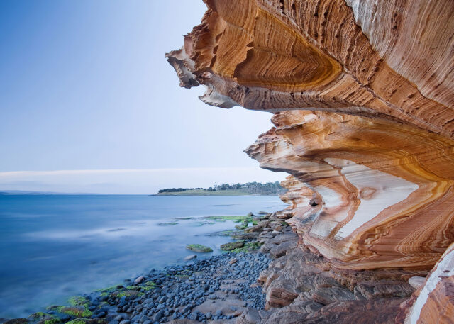 Australian coast: sandstone cliffs, blue sea, tree-lined horizon.