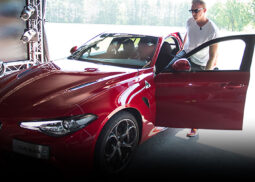 Man in sunglasses beside red Alfa Romeo.