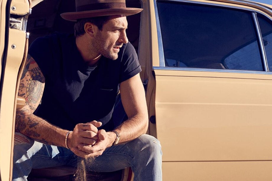 Man in hat sits by beige car.