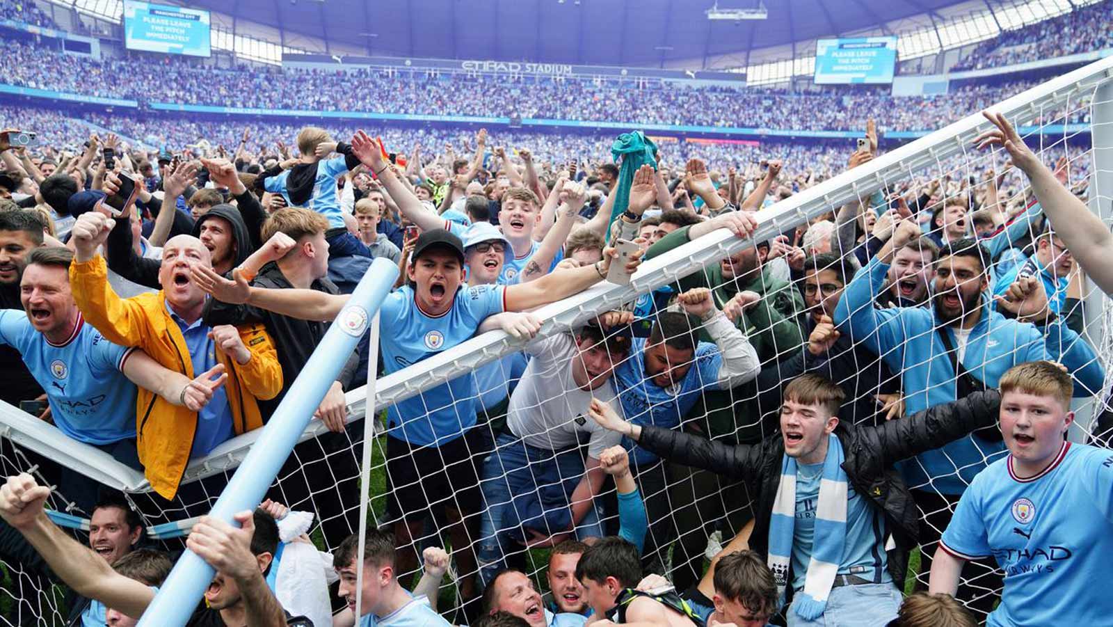 Fans in light blue jerseys celebrate around goalpost.