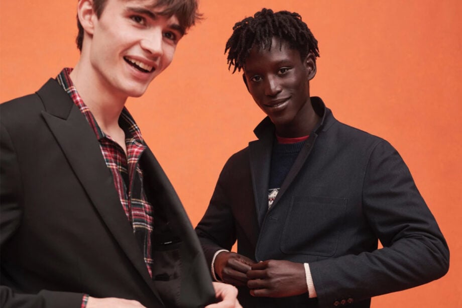 Two men in suits against orange backdrop.