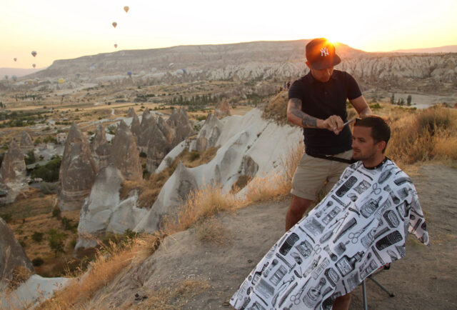 Nomad Barber gives outdoor haircut with scenic view.
