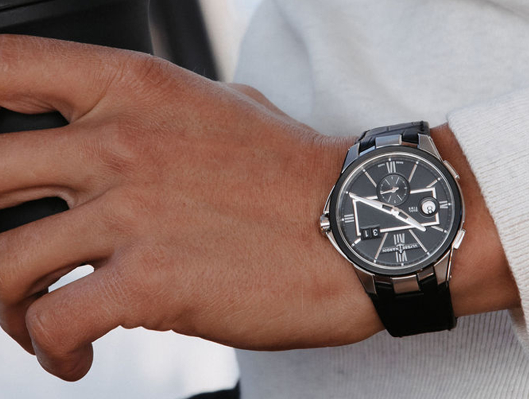 Wearing Ulysse Nardin watch, holding black cup.
