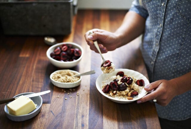 Person enjoys oatmeal with cherries and nuts.