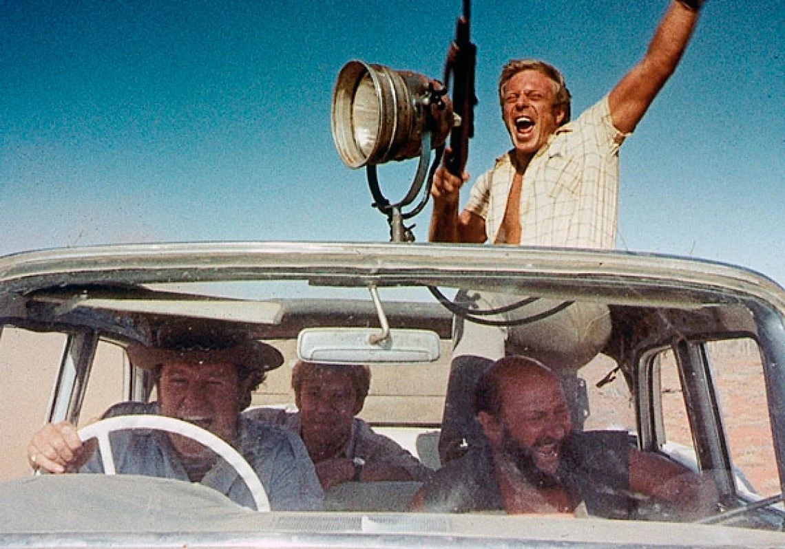 A frame from 'Wake In Fright' of men driving through the Outback